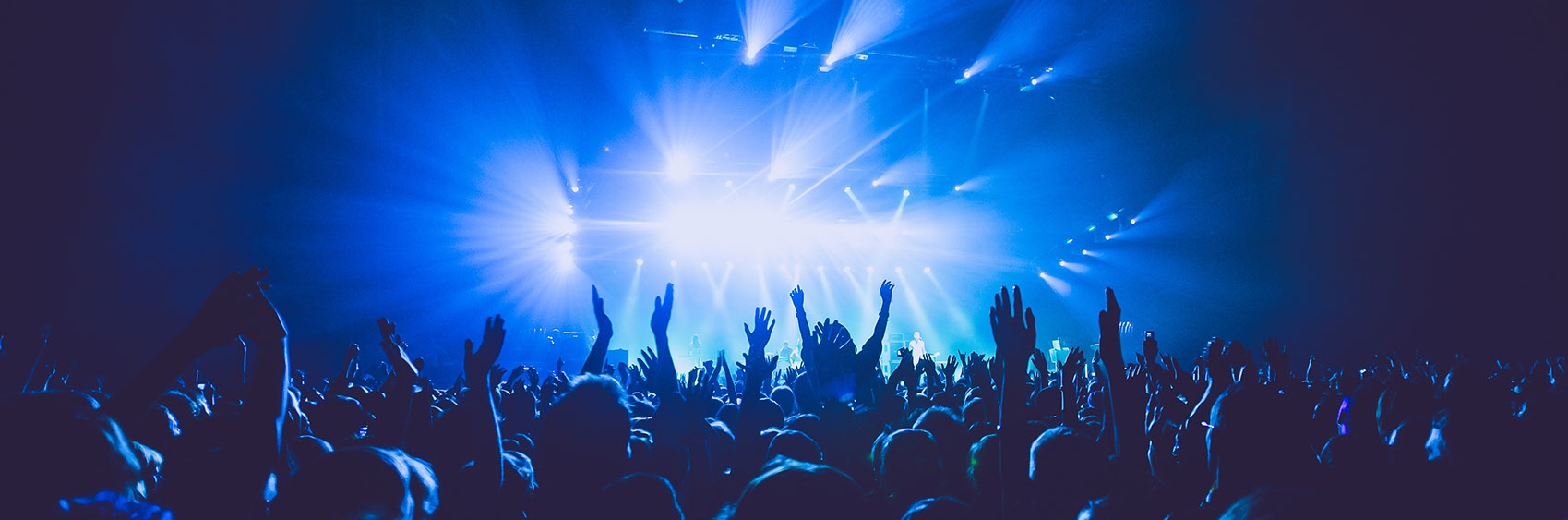 A crowded concert hall with scene stage lights in blue tones, rock show performance, with people silhouette, on dance floor air during a concert festival